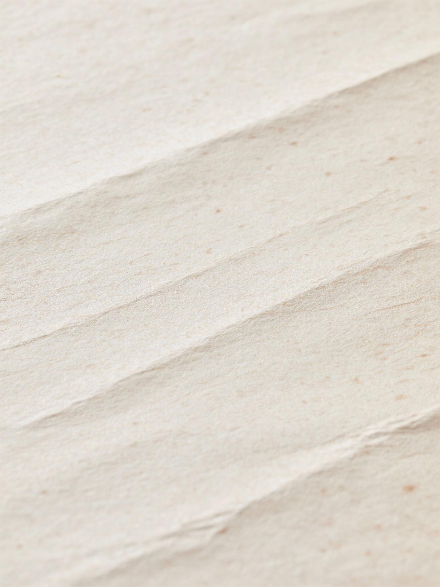 High resolution seamless paper texture, off-white sheet, subtle grain, soft creases, flatbed scanner effect with light vignette and faint dust specks, minimal colour variation, suitable for print packaging background